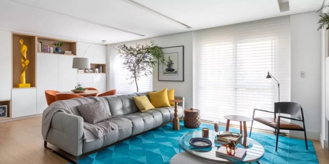 A ampla entrada de luz natural serviu de pontapé para a reforma do apê. A base neutra, além de ampliar a iluminação, permite que os detalhes coloridos, como o tapete azul vibrante e os objetos decorativos, se destacam sem sobrecarregar o espaço | Projeto do escritório Rawi Arquitetura + Design | Foto: Alexandre Disaro