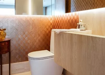 Neste lavabo, a bancada com cuba esculpida foi toda trabalhada no mármore travertino romano estucado, acompanhando o mesmo material do piso, rodapé e paredes para trazer integração visual. Além disso, as profissionais utilizaram o recurso de colocar a torneira na lateral para aumentar o comprimento da cuba até a parede | Projeto Dantas & Passos Arquitetura | Foto: Maura Mello
