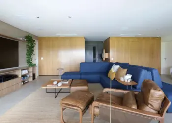 No living deste apartamento, com projeto de reforma de Marí Aní Oglouyan, os painéis de madeira da SCA Jardim Europa ‘vestem’ as paredes principais, desde o hall, e ainda escondem a porta mimetizada do lavabo | Foto: Mariana Orsi
