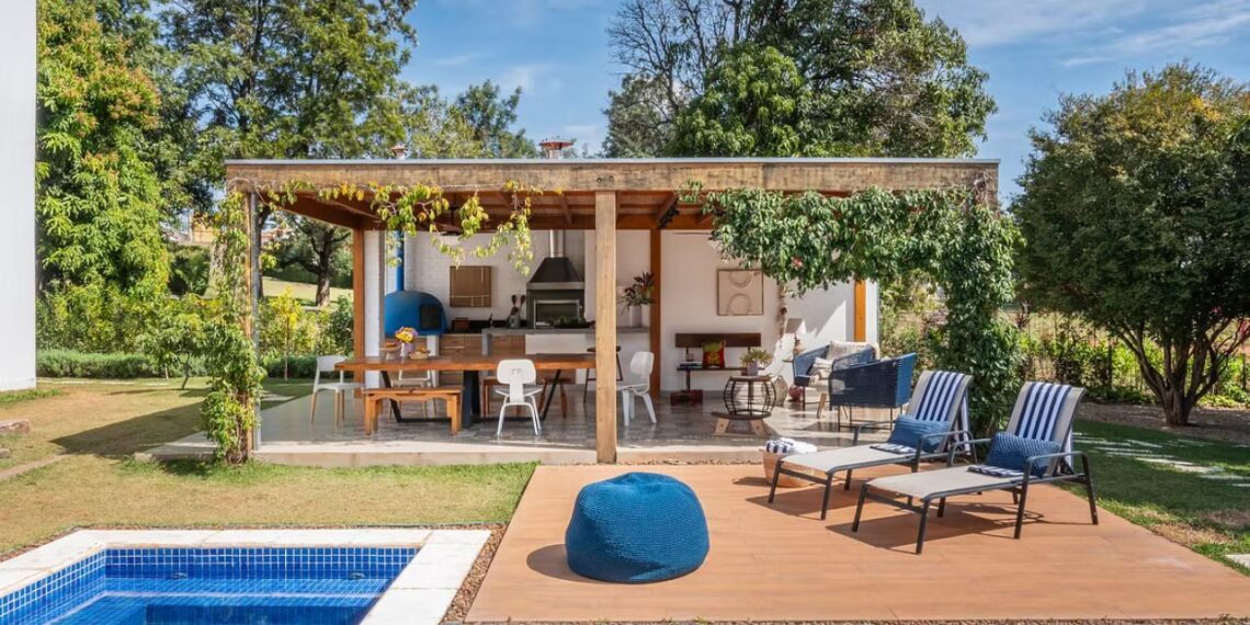 Área externa com piscina, deck amadeirado e espreguiçadeiras integradas à área gourmet em casa revitalizada no interior de São Paulo.