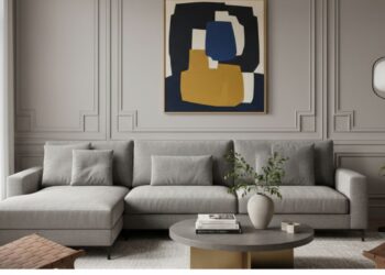 Sala sofisticada com boiserie na sala de estar em tom neutro que emoldura o sofá em “L” e valoriza a obra de arte. A composição equilibra arquitetura clássica e décor contemporâneo, criando um ambiente elegante, acolhedor e visualmente harmônico.